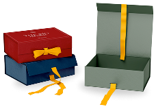 Three rectangular gift boxes are shown: a red box stacked on a blue one, both tied with yellow ribbons, and an open green box with a yellow ribbon beside them—perfect for showcasing branded products or custom merchandise.