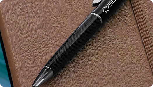 A black pen with silver accents, ideal for branded products, rests diagonally on a textured brown notebook cover. The pen features a subtle patterned grip and a visible logo near the clip.